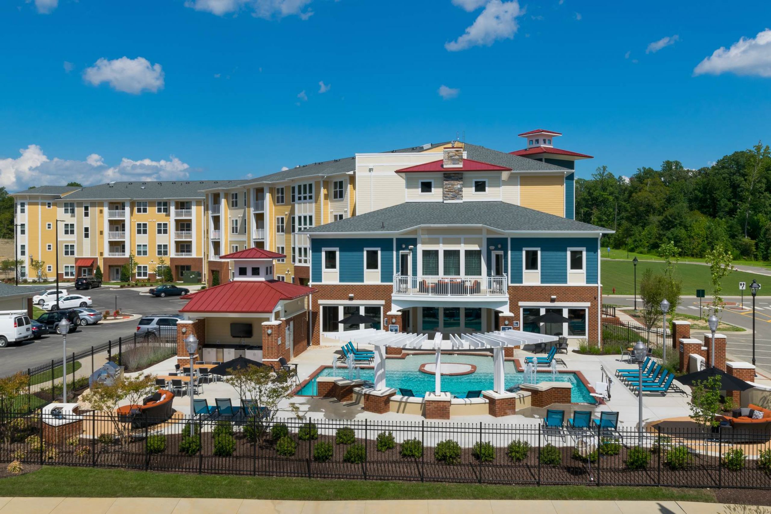 Attain at Quarterpath apartment homes with Modern apartment complex with a central pool, lounge chairs, and landscaped grounds under a blue sky.