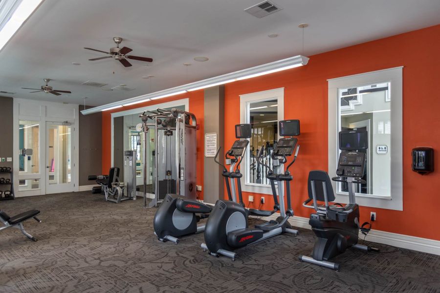 Attain at Quarterpath apartment homes with A gym with treadmills, elliptical machines, weight equipment, and mirrors on an orange accent wall.