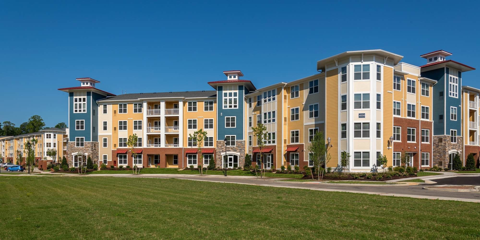 Attain on 5th apartment homes with Colorful modern apartment building with multiple floors, large windows, and a neatly landscaped lawn in front.