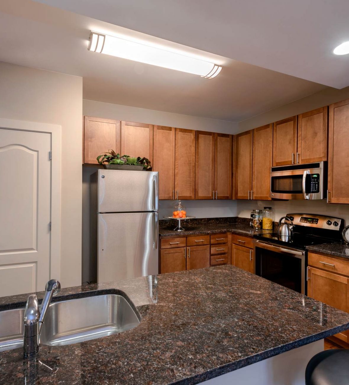 Attain at Quarterpath apartment homes with Modern kitchen with wooden cabinets, stainless steel appliances, and a granite island with a sink.