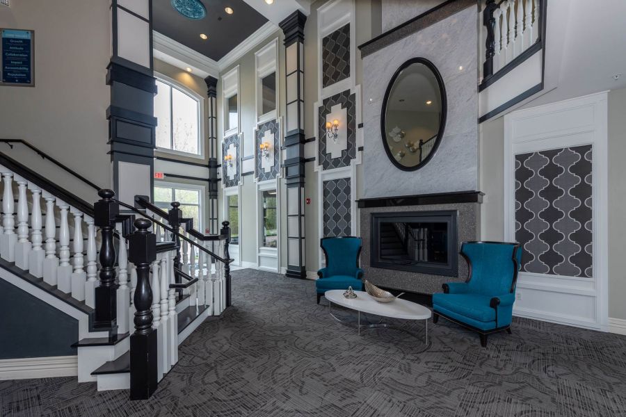 Attain at Quarterpath  apartment homes with Modern lobby with a staircase, fireplace, two blue chairs, and large windows letting in natural light.