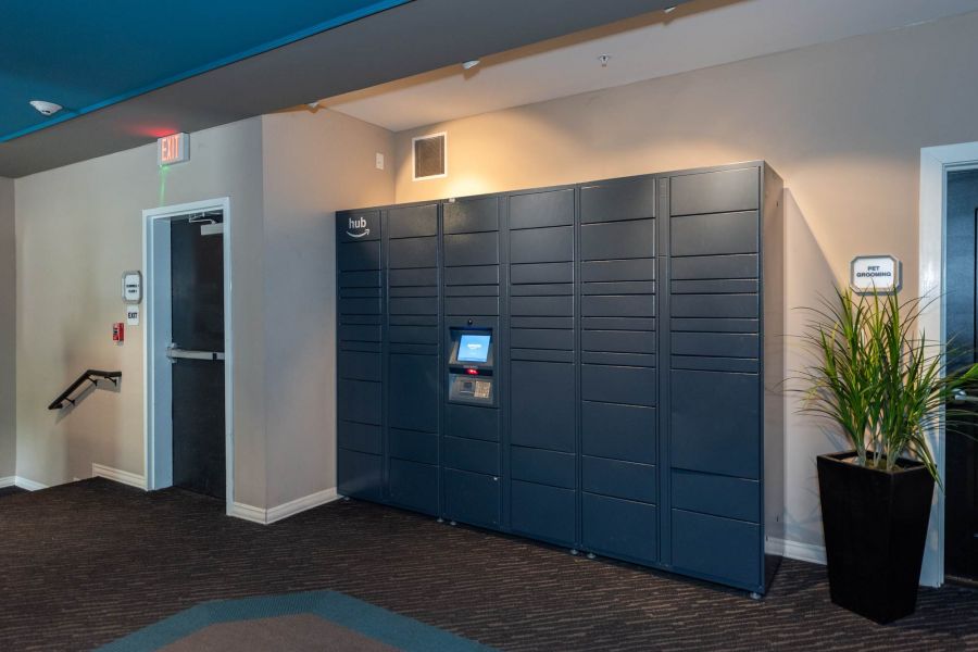 Attain at Quarterpath  apartment homes with Blue package locker system with a touchscreen, in a hallway near a door and a potted plant.