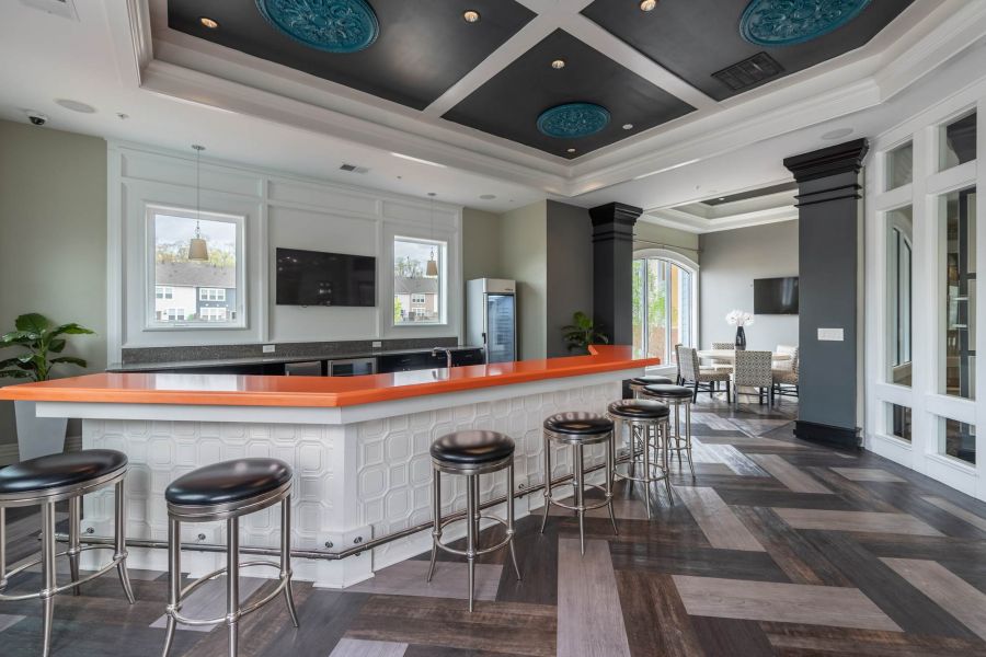 Attain at Quarterpath apartment homes with Modern lounge with an orange bar counter, black stools, TV, and patterned wood flooring.
