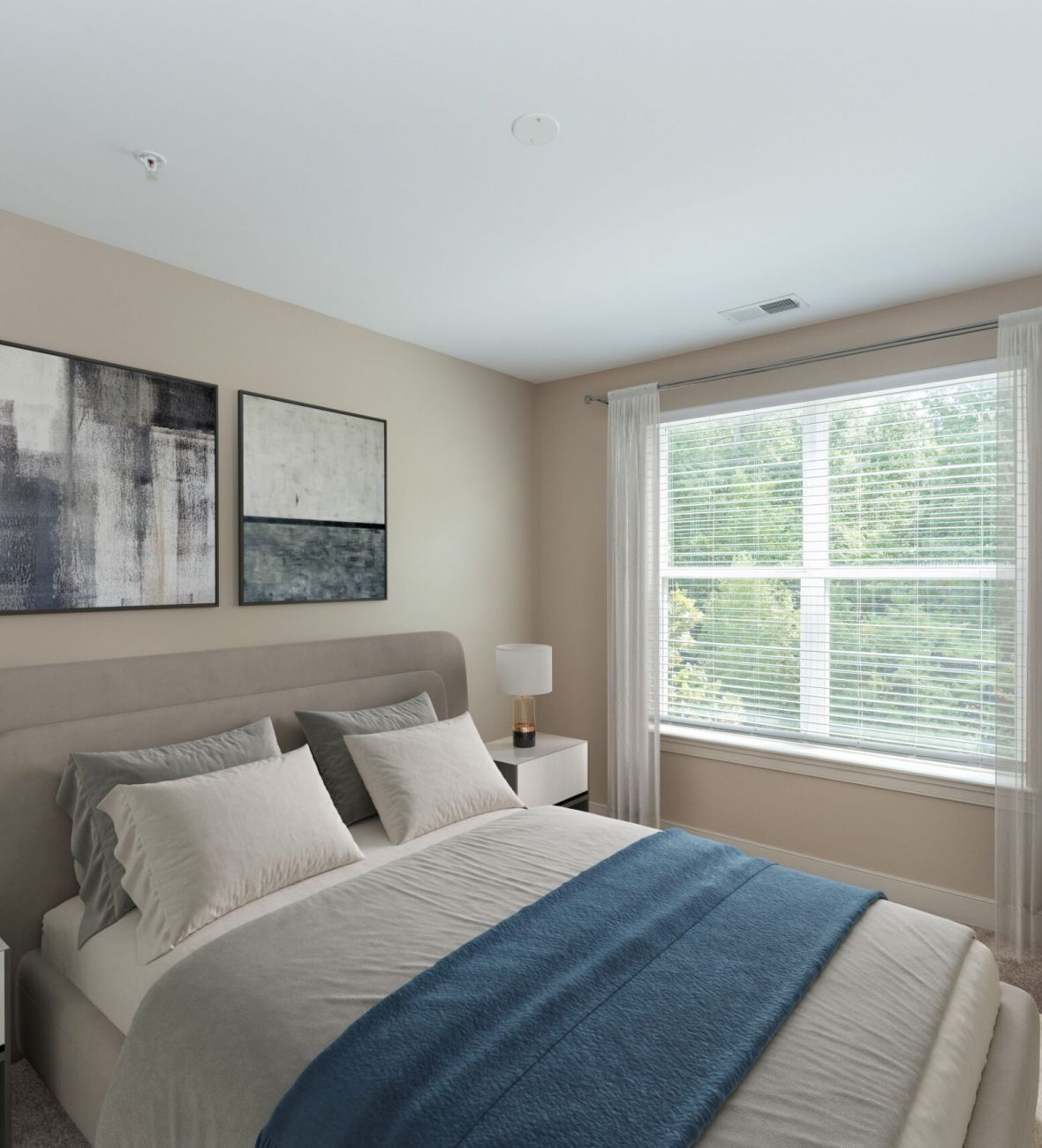 Attain on 5th apartment homes with Modern bedroom with beige walls, a bed with gray and blue bedding, two nightstands, and a large window with sheer curtains.