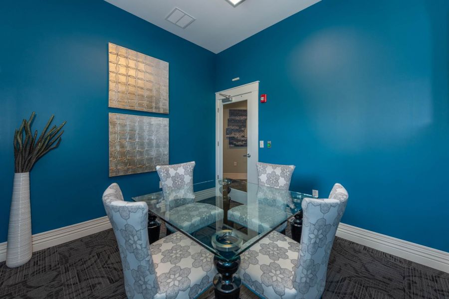 Attain at Quarterpath  apartment homes with Small meeting room with blue walls, glass table, four floral chairs, and modern silver wall art.