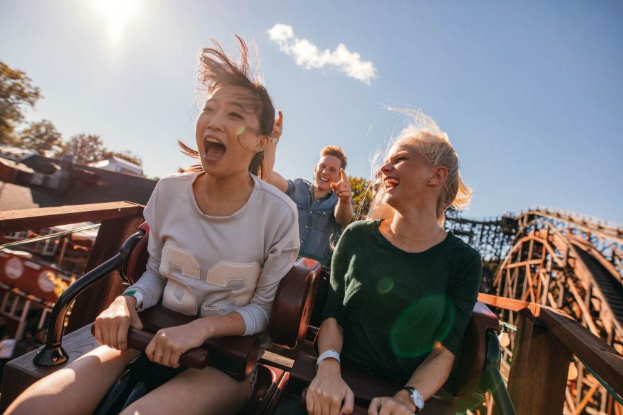 Attain at Quarterpath apartment homes with Two women laughing and enjoying a roller coaster ride with another person in the background on a sunny day.