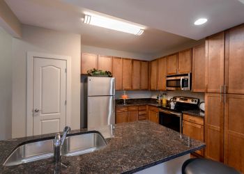 Attain at Quarterpath apartment homes with Modern kitchen with wooden cabinets, stainless steel appliances, and a granite island with a sink.