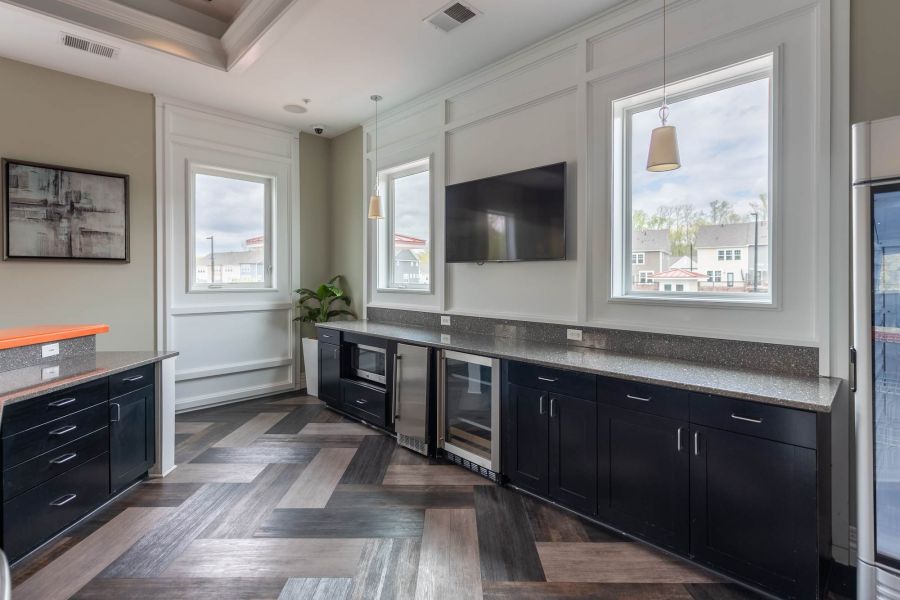 Attain at Quarterpath apartment homes with Modern kitchen with dark cabinets, large windows, wall-mounted TV, and herringbone-patterned floor.